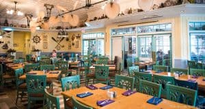 Nautical eatery with teal chairs, wooden tables, ocean accents; Disney World vibes, relaxed and nearly empty dining area.