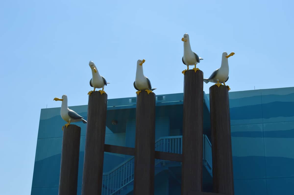 Four seagull statues on wooden posts evoke Disney Springs vibes, set against a blue building and sky—great for theme park fans.