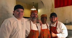 Four Disney chefs, three in bright aprons and hats, smiling together backstage like Cast Members about to share top theme park tips.