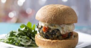 A cheesy veggie burger on a bun with green salad, plated and ready for hungry Disney park-goers craving a delicious snack.