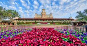 Vibrant flowers bloom before the iconic Magic Kingdom castle and clock tower beneath a sunny sky, embodying Disney World’s wonder.