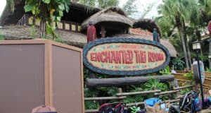 Enchanted Tiki Room entrance sign at Magic Kingdom, framed by strollers and tropical plants, a Disney World fan favorite.