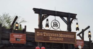 Entrance sign for Big Thunder Mountain Railroad at a theme park, with lanterns hanging and a wait time display reading "40 minutes." Red Mickey Mouse balloons are visible in the foreground.