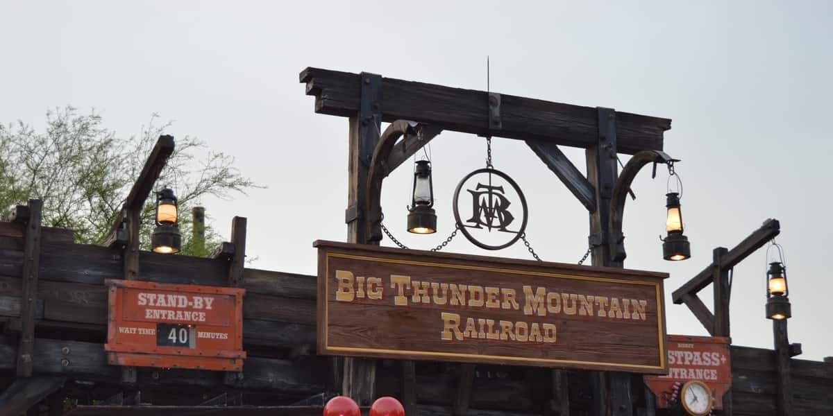 Entrance sign for Big Thunder Mountain Railroad at a theme park, with lanterns hanging and a wait time display reading "40 minutes." Red Mickey Mouse balloons are visible in the foreground.