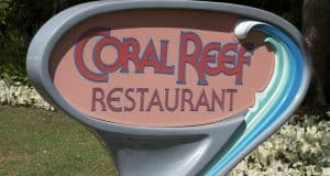 Coral Reef Restaurant sign with aquatic theme stands by vibrant gardens, welcoming Epcot guests for an underwater dining adventure.