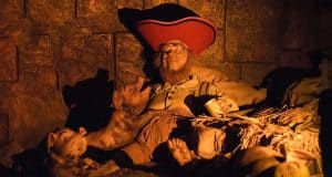 A Pirates of the Caribbean animatronic relaxes on hay with pigs under warm lighting, evoking classic Disney park charm.