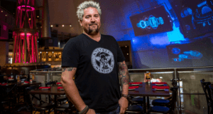 A stylish guest with spiked hair and tattoos inside Planet Hollywood Observatory, vibrant lights shining above empty dining tables.