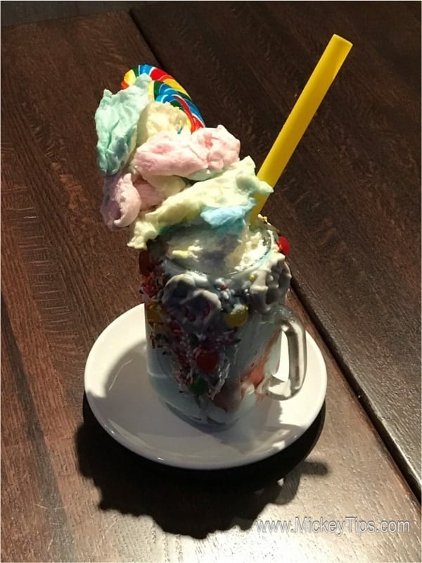 Planet Hollywood Observatory’s vibrant milkshake, loaded with cotton candy, lollipop, and yellow straw—a Disney Springs delight!.