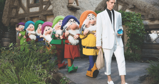 A stylish guest in a white suit strolls past the Seven Dwarfs by their cottage, during a GQ Style photo shoot in Fantasyland.