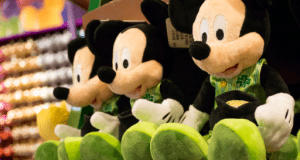 Festive Mickey Mouse plushies in shamrock outfits line a Disney Springs shelf, ready for St. Patrick’s Day celebrations.