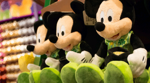 Festive Mickey Mouse plushies in shamrock outfits line a Disney Springs shelf, ready for St. Patrick’s Day celebrations.