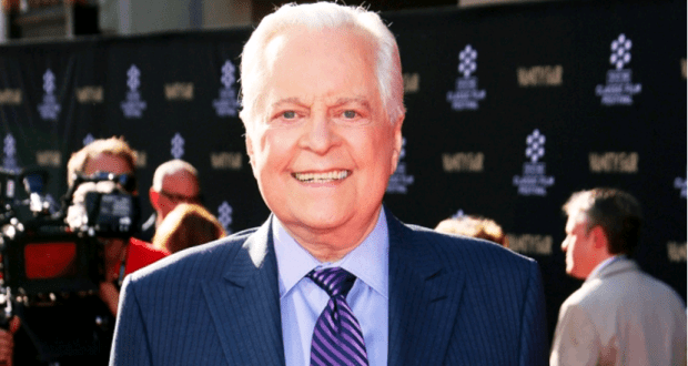 Robert Osborne-style host beaming in a suit on the red carpet, with entertainment fans and press capturing the Hollywood moment.