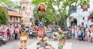 Stilt dancers in vibrant costumes entertain guests amid a lively village scene, embodying the festive magic of Disney World.