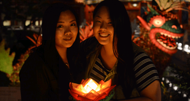 Celebrate at Epcot China Pavilion as two friends share a glowing lotus lantern before the vibrant dragon statue—PhotoPass ready!.
