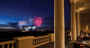 Guests savor dinner on an open-air terrace as vibrant fireworks light up the sky, capturing the magic of a Walt Disney World night.