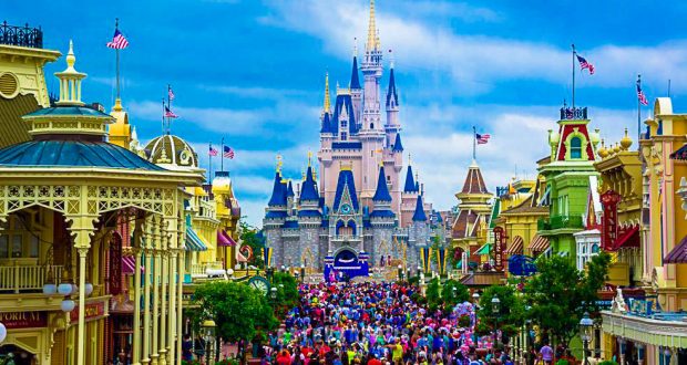 Guests fill Main Street USA at Disneyland, gathering beneath Sleeping Beauty Castle and vibrant buildings on a sunny afternoon.