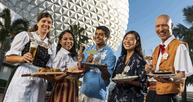 Festival-goers in vibrant attire enjoy global bites and drinks outside EPCOT’s geodesic dome, celebrating Food & Wine Fest fun.