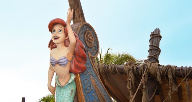 Ariel, the Little Mermaid, perched on a ship’s prow, delights Magic Kingdom guests beneath the iconic Florida sunshine.