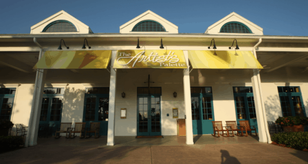 The Artist's Palette entrance at Walt Disney World, featuring blue doors and a cheerful yellow sign under sunny skies.