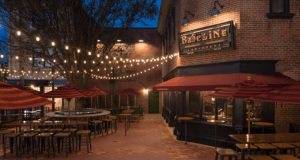 BaseLine Tap House outdoor patio at Disney World, glowing string lights, red umbrellas, and casual seating as evening sets in.