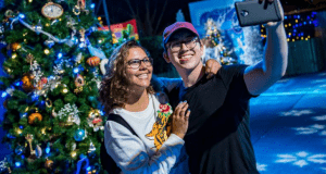 Guests snap a festive selfie by a sparkling Christmas tree along the magical Christmas Tree Trail at Walt Disney World.