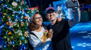 Guests snap a festive selfie by a sparkling Christmas tree along the magical Christmas Tree Trail at Walt Disney World.