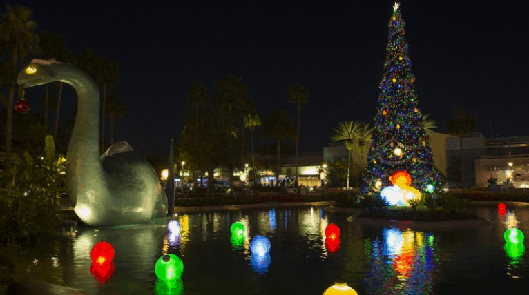 Christmas tree and Dino statue aglow with lights shimmer on the lake, channeling Disney World’s festive nighttime spectacle.
