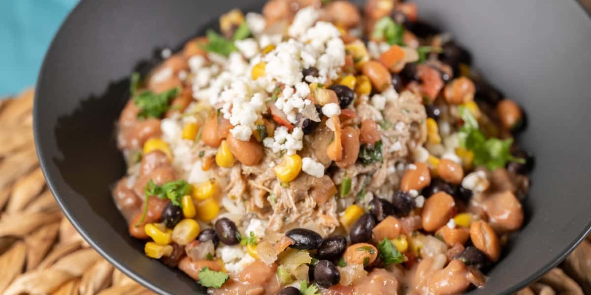 A black bowl filled with a colorful mix of shredded meat, pinto and black beans, corn, cilantro, and crumbled cheese on white rice—proof that not all dishes belong among the Worst Quick Service Restaurants at Disney World.