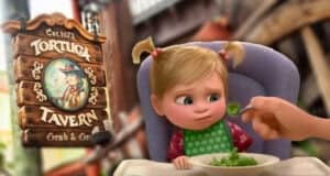 A young child with pigtails sits in a high chair, frowning at a spoonful of broccoli. Beside her, a wooden sign reads “Tortuga Tavern Grub & Grog”—one of the Worst Quick Service Restaurants at Disney World—featuring a pirate illustration.
