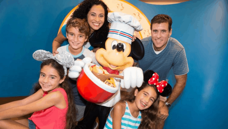 Smiling family with Mickey Mouse at Disney World, girls in mouse ears, captured by PhotoPass for a magical memory.