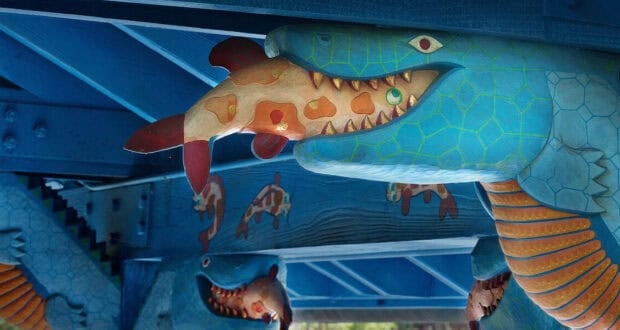 A close-up of a blue, snake-like creature sculpture with a painted fish in its mouth, part of the vibrant animal-themed decor at Flame Tree Barbecue, featuring turtle designs and other whimsical sculptures in the background.