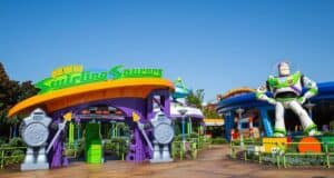 Entrance to the "Alien Swirling Saucers" ride at a theme park, featuring colorful structures and a large statue of a space ranger character. Bright signage and playful design elements create a whimsical atmosphere.