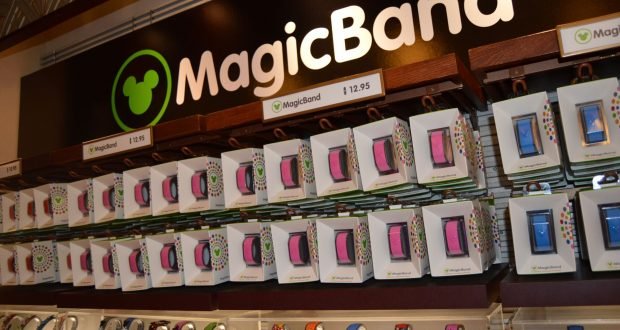 MagicBands in a rainbow of Disney designs line the shelves beneath a MagicBand sign, ready for your next park adventure.