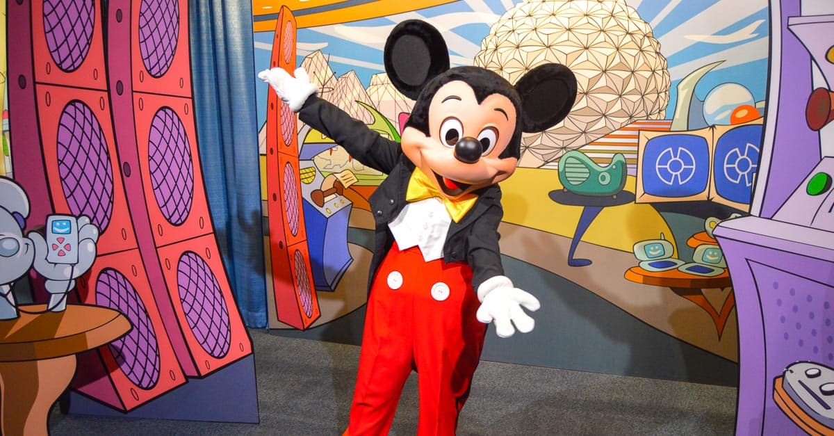 Mickey Mouse welcomes guests with open arms in front of a vibrant, whimsical backdrop at Disney World, radiating pure magic.