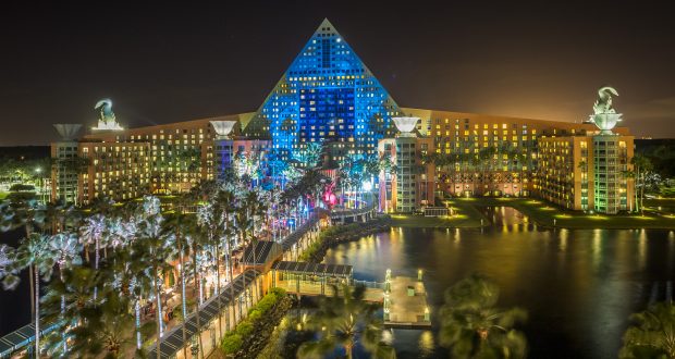 Swan and Dolphin aglow at night, vibrant lights dancing on water, palm trees, and festive energy of Disney's Food & Wine Classic.