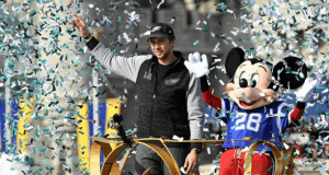 Mickey Mouse and a friend wave from a festive parade float at Walt Disney World, surrounded by celebratory confetti.