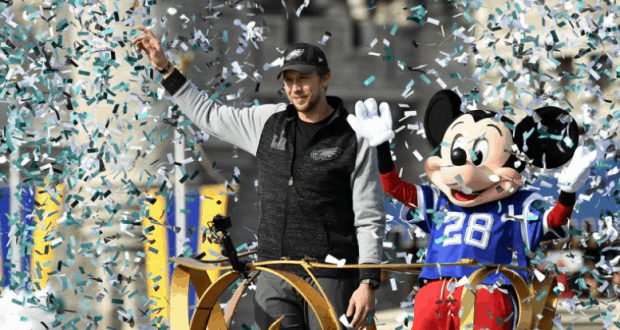 Mickey Mouse and a friend wave from a festive parade float at Walt Disney World, surrounded by celebratory confetti.