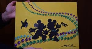 Mickey and Minnie Mouse silhouettes with Mardi Gras beads evoke Port Orleans flair, set on a vibrant yellow backdrop at Disney World.
