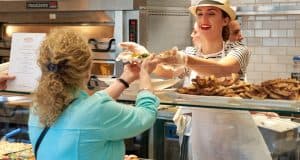 At Disney Springs, a cheerful Pizza Ponte team member serves up a pizza slice to guests, adding fun to National Pizza Day magic.