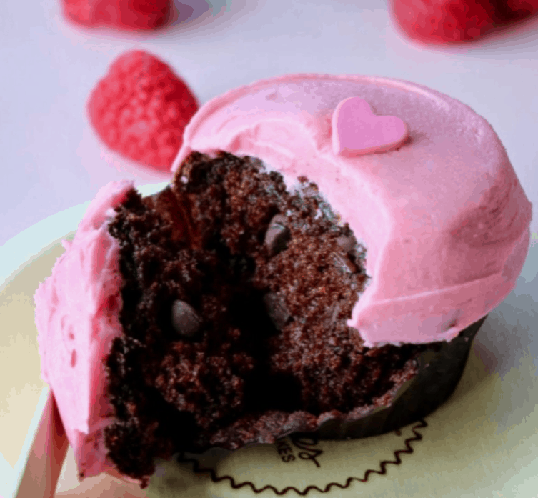 Valentine’s-themed chocolate cupcake with pink frosting and a heart, enjoyed at Main Street Bakery, Magic Kingdom—sprinkles, raspberries.