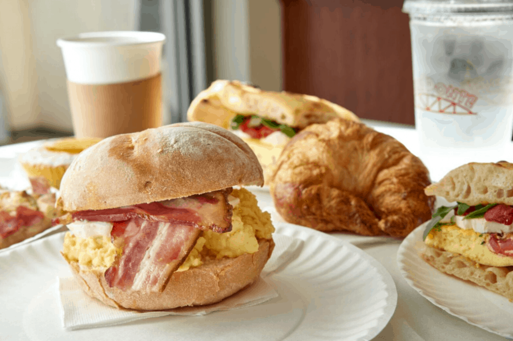 Egg and bacon breakfast sandwiches, a croissant, and coffee served on white plates at Disney Springs to fuel your Disney day.