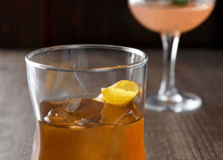 Whiskey on the rocks with a lemon twist at The Edison, Walt Disney World, alongside a vibrant pink cocktail—Dapper Day perfection.