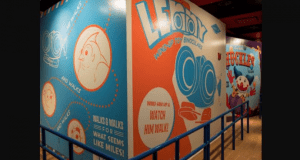 Toy Story Mania’s vibrant, cartoon-style walls pop with playful graphics of Chuckles and Lenny, framed by bright blue railings.