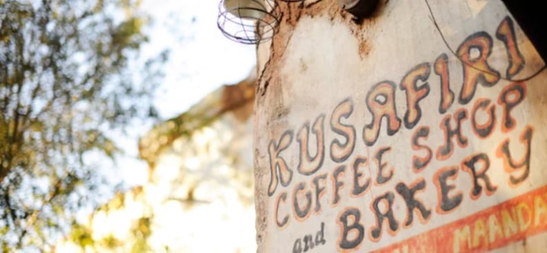 Rustic Kusafiri Coffee Shop and Bakery sign at Disney’s Animal Kingdom, surrounded by lush trees and warm sunlight.