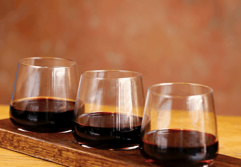 Trio of red wines on a wooden tray at Maria & Enzo's in Disney Springs, set on a rustic table—cheers to National Wine Day!.
