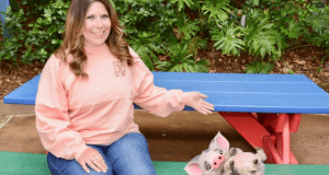Guest delights in a Magic Shot at Walt Disney World, pointing at plush Pua and Piglet toys, with greenery and a blue table behind.
