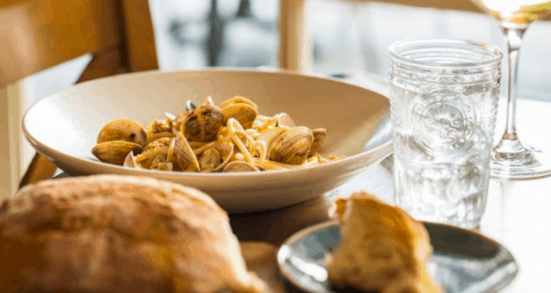 Classic Italian fare at Terralina Crafted Italian in Disney Springs—a bowl of clams pasta, crusty bread, water, and wine.