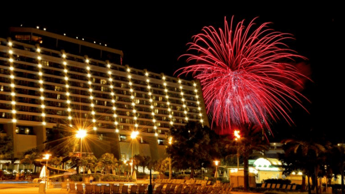 Red fireworks explode above Disney’s Contemporary Resort, illuminating palm trees and empty seats on a sparkling New Year’s Eve.