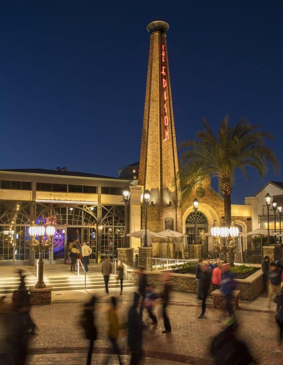 Guests stroll past The Edison at Disney Springs, its iconic neon sign glowing against the vibrant night entertainment scene.
