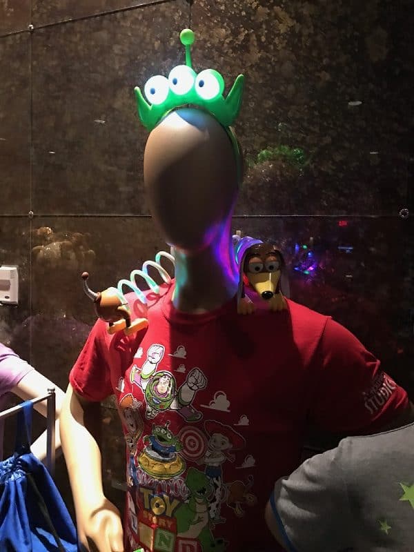 Toy Story Land mannequin sports a glowing alien headband, Buzz tee, plus Slinky Dog and Woody toys—perfect souvenir showcase.